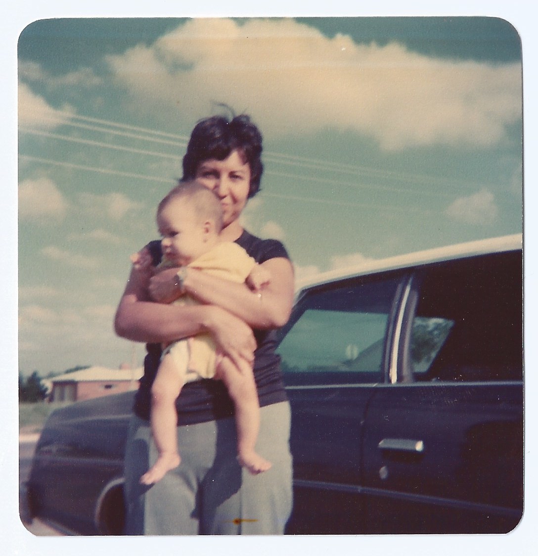 mom holding me as a baby in front of car